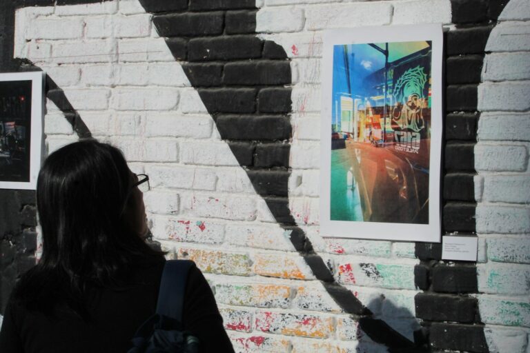 Person views colorful artwork on a brick wall with shadows.