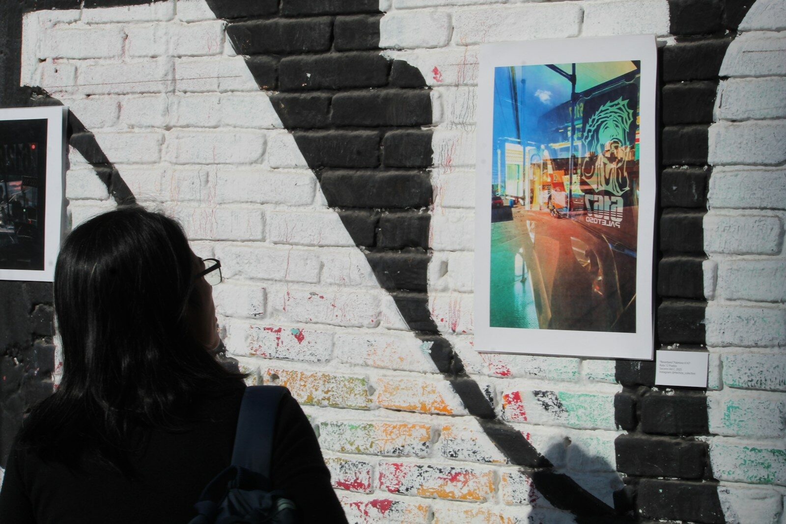 Person views colorful artwork on a brick wall with shadows.